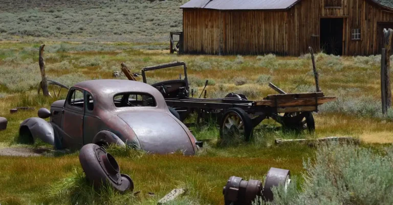Weathered old car sitting unused in a grassy field beside a wooden barn