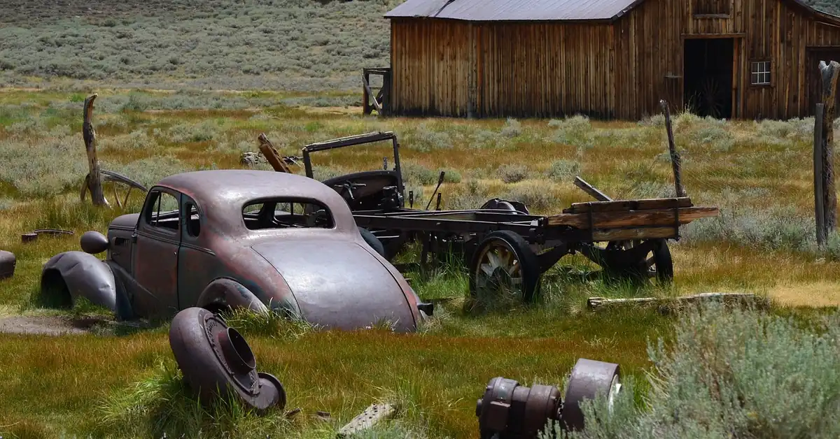 Weathered old car sitting unused in a grassy field beside a wooden barn