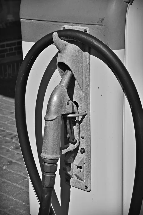 Black and white photo of a vintage gasoline nozzle hanging on its pump