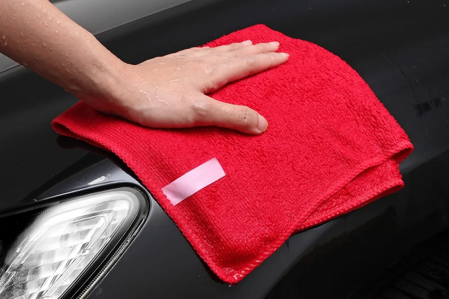 Hand wiping a wet black car panel with a red microfiber cloth Hand wiping a wet black car panel with a red microfiber cloth