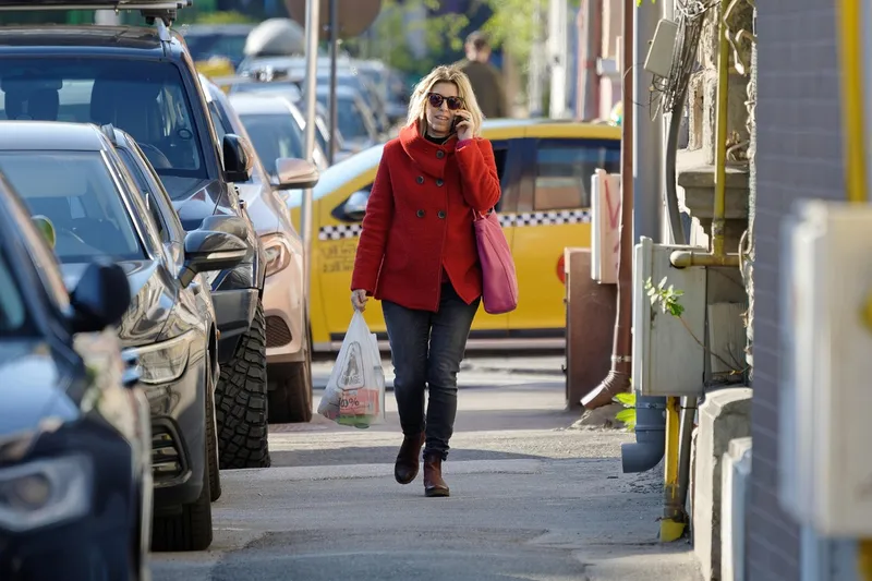 Woman on a phone call walking along a street of parked cars