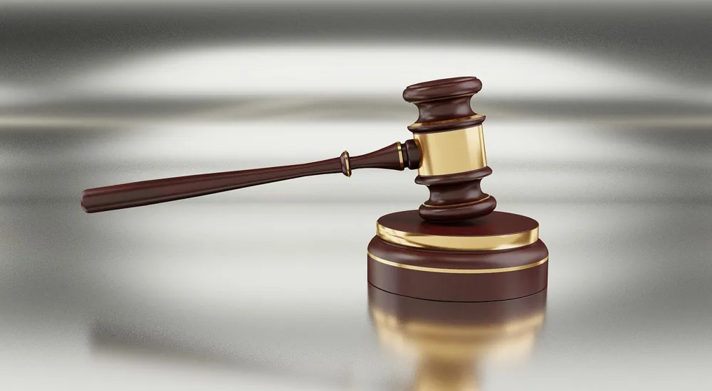 Wooden judge gavel with gold bands resting beside its sound block on a polished surface