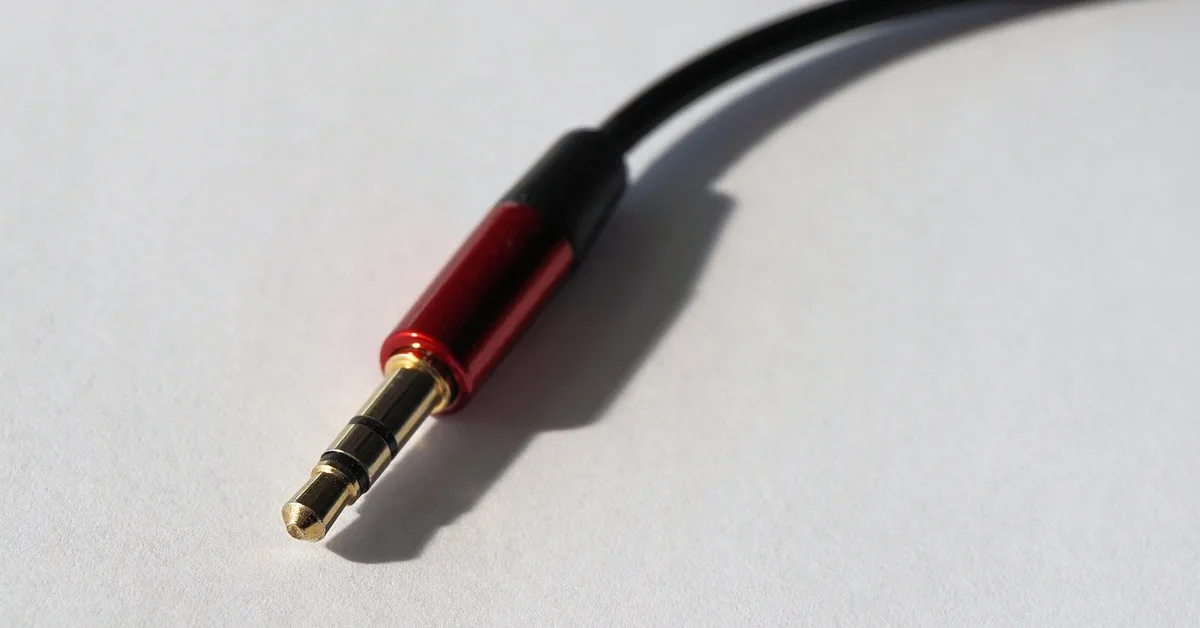A 3.5mm audio plug with a red and gold metal barrel and black cable on a white surface