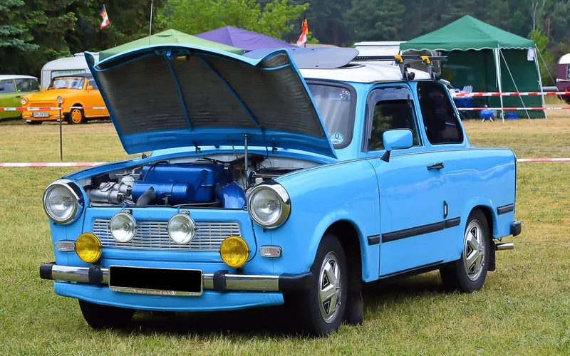 Small blue car with its hood open on grass