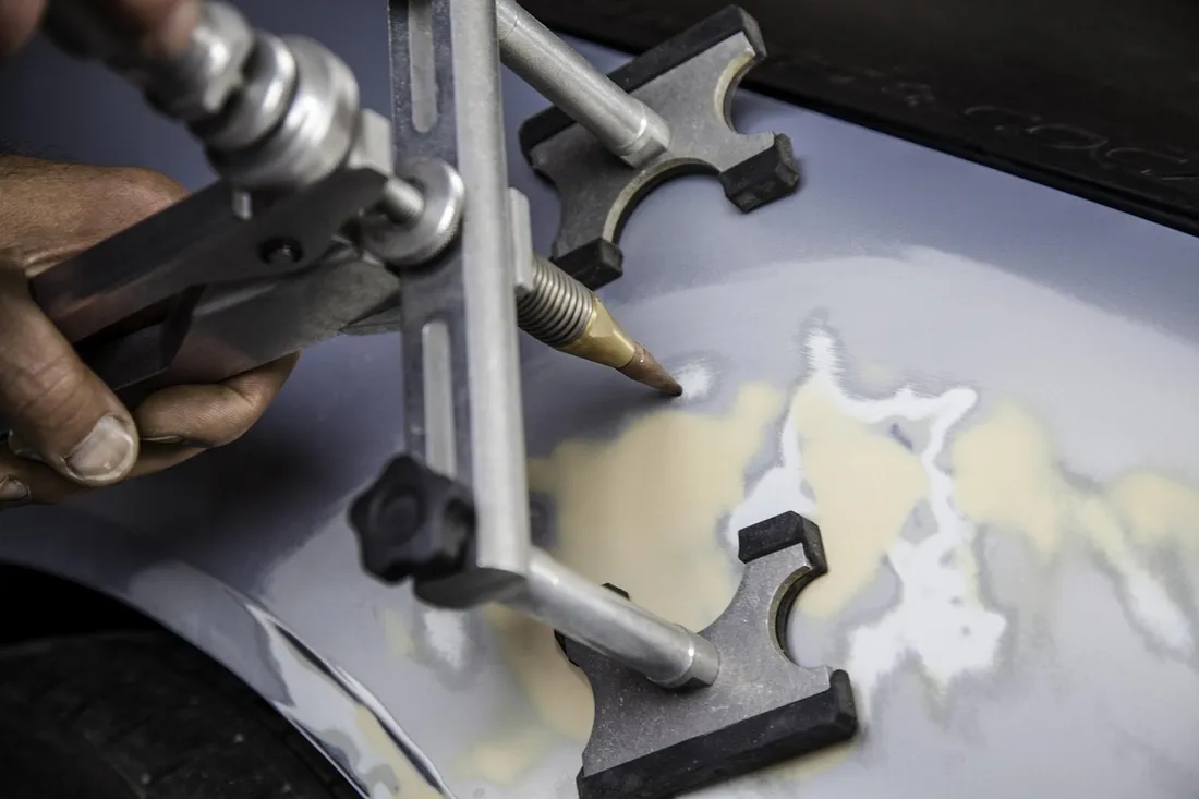 Bridge-style dent puller set on a car panel in a body shop