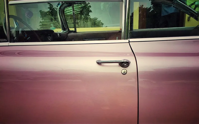 Exterior door handle and small key lock on the door of an older pink car