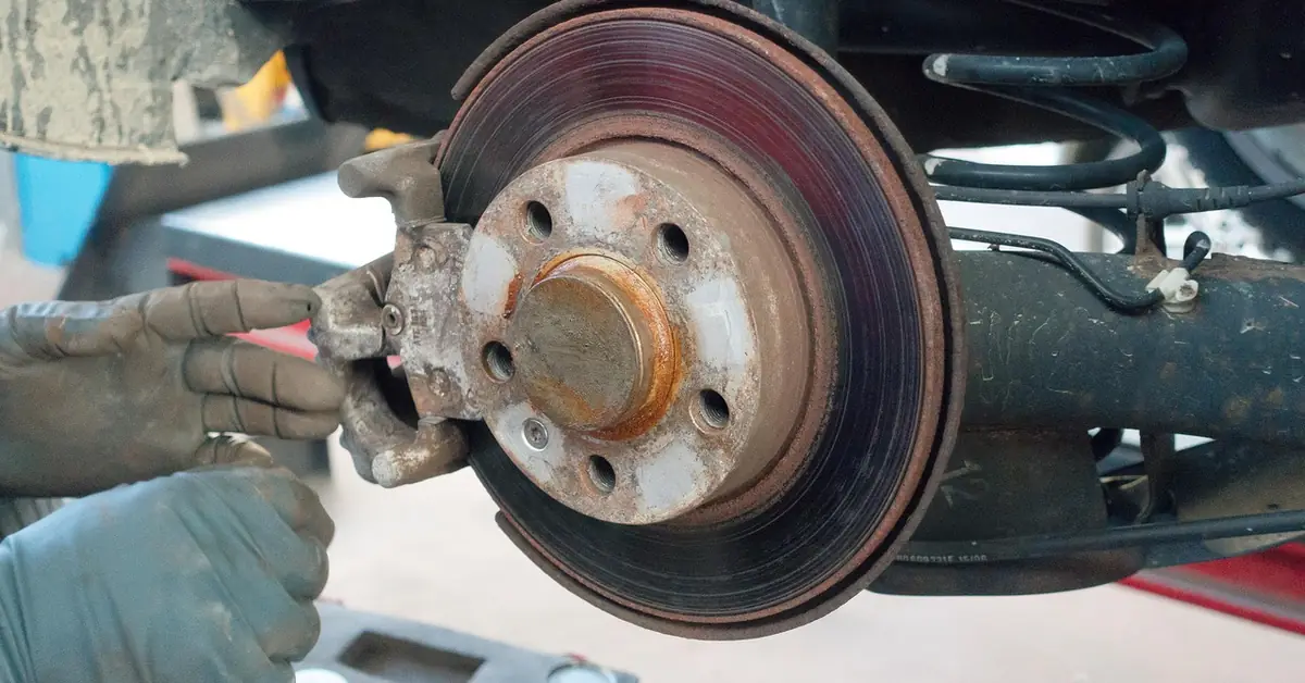 Rear suspension of a car on a lift with a coil spring, axle beam and brake disc visible