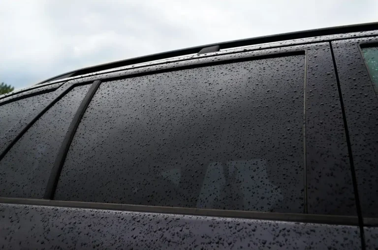 dark tinted rear side window of an SUV covered in water drops