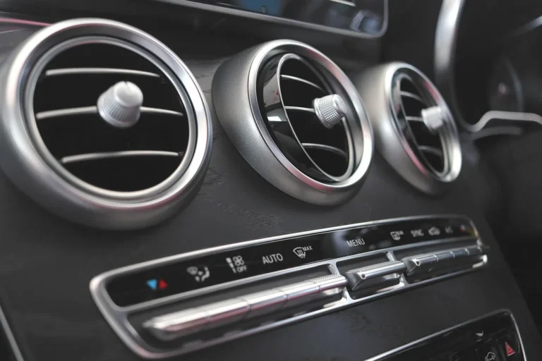 Three round dashboard air vents above a climate control button strip in a car