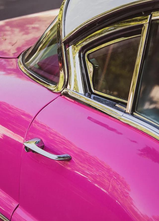 Chrome exterior door handle on the rear door of a pink vintage car