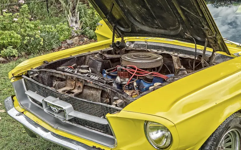 Classic yellow car with its hood propped open over the engine bay