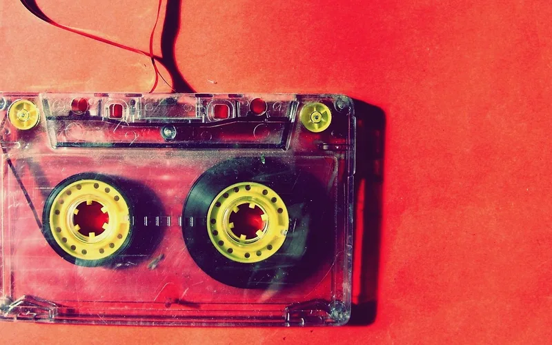 Clear-shell audio cassette tape with yellow hubs lying on a red surface
