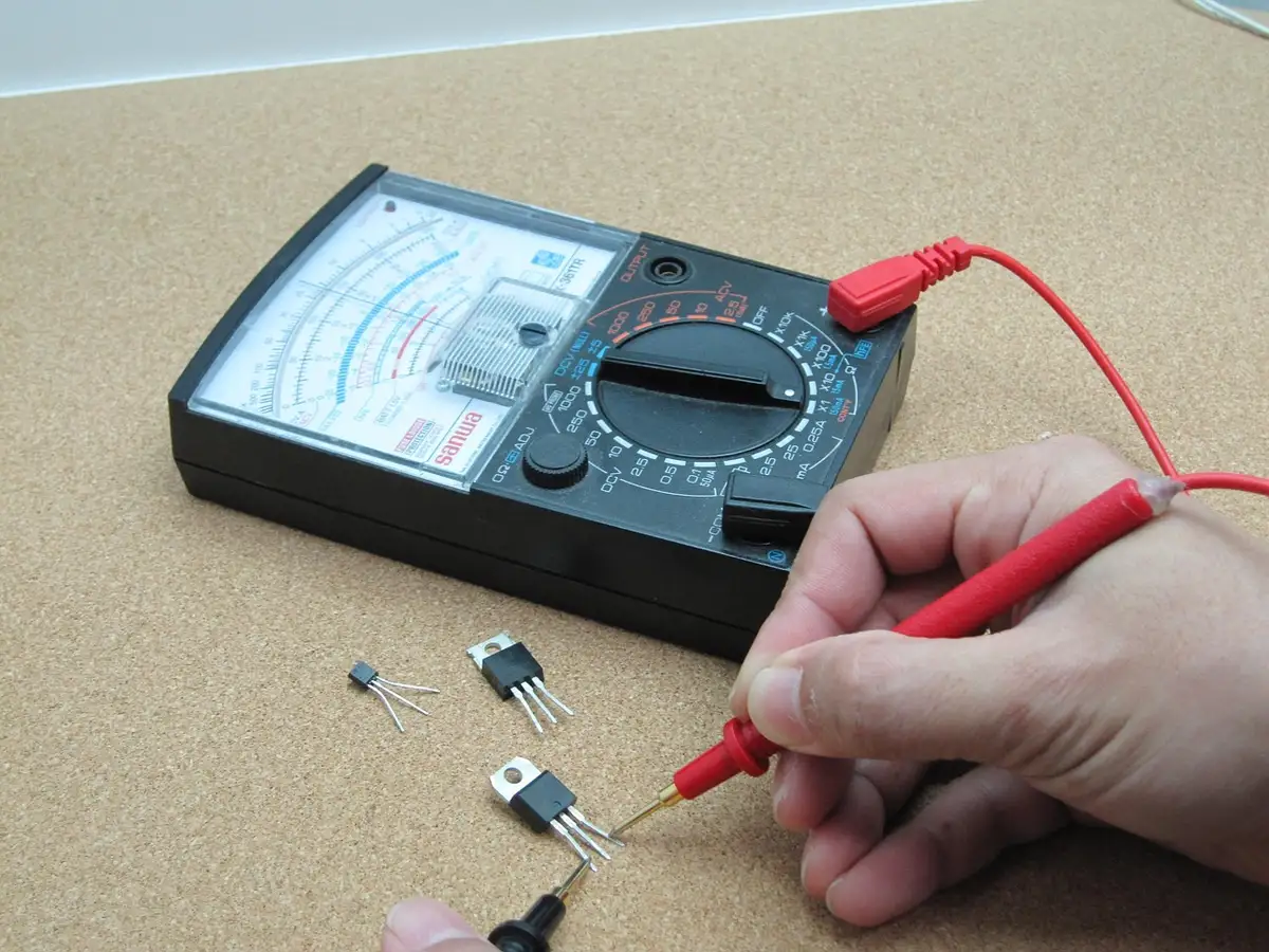 Analog multimeter with red and black test leads held by a hand