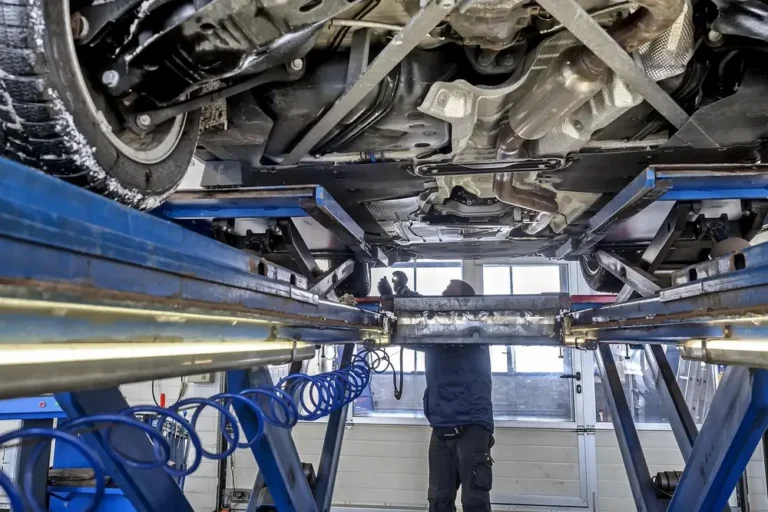 Underside of a vehicle raised on a lift in a workshop with a person standing beneath it