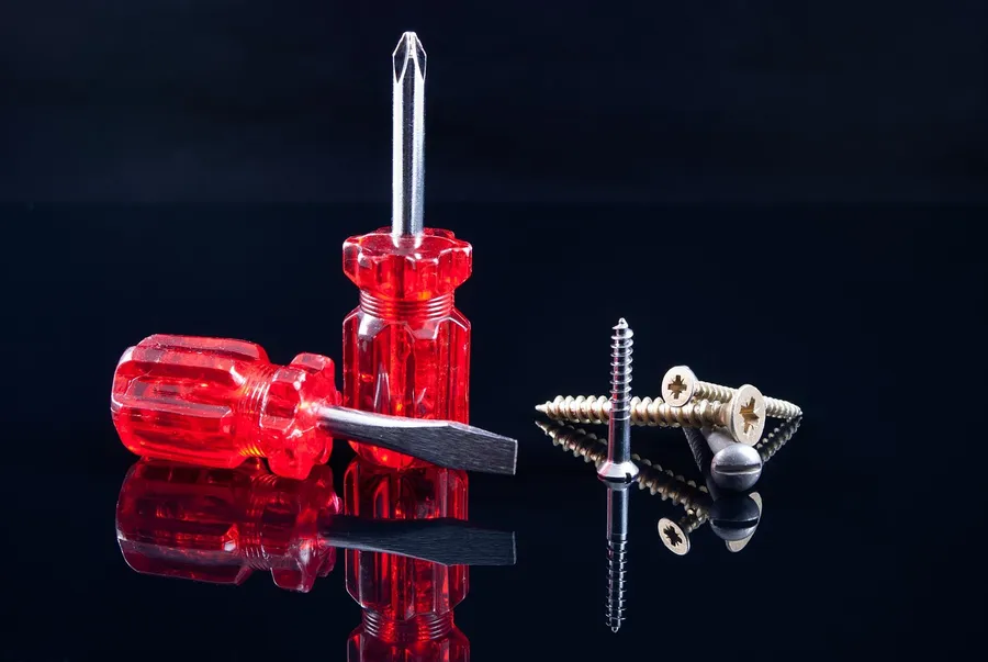 A Phillips and a slotted screwdriver with wood screws on a black reflective surface