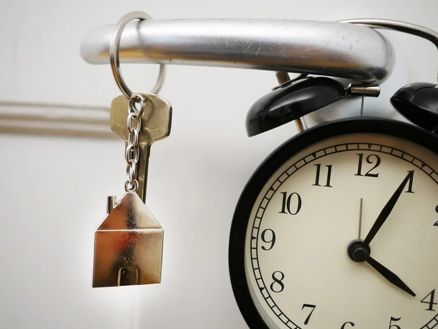 A house key with a house-shaped keychain hanging beside an alarm clock