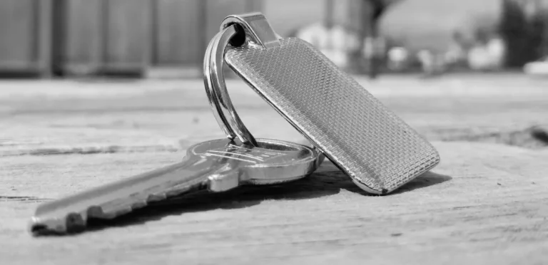 A metal key on a key ring with a textured metal tag lying on a wooden surface