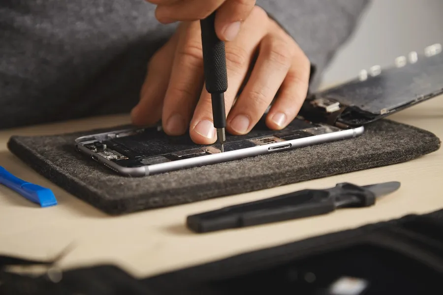 Hands using a small screwdriver on a small electronic device laid on a felt mat