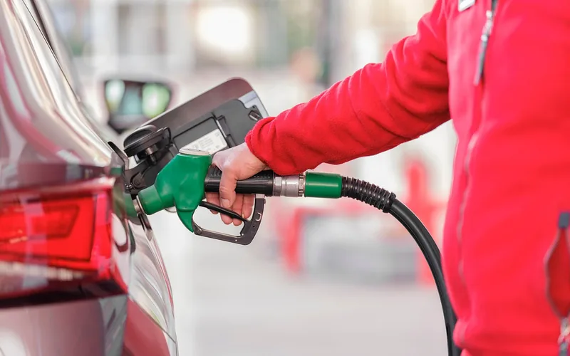 Driver standing at the pump while refueling a car at a gas station Driver standing at the pump while refueling a car at a gas station