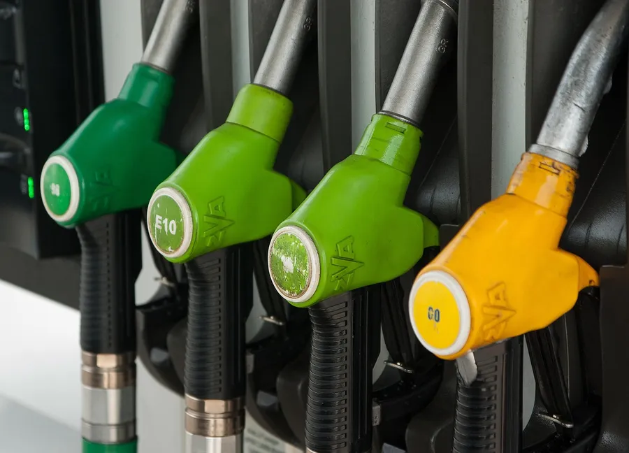 Four fuel dispenser nozzles in green and yellow hanging side by side at a fuel pump