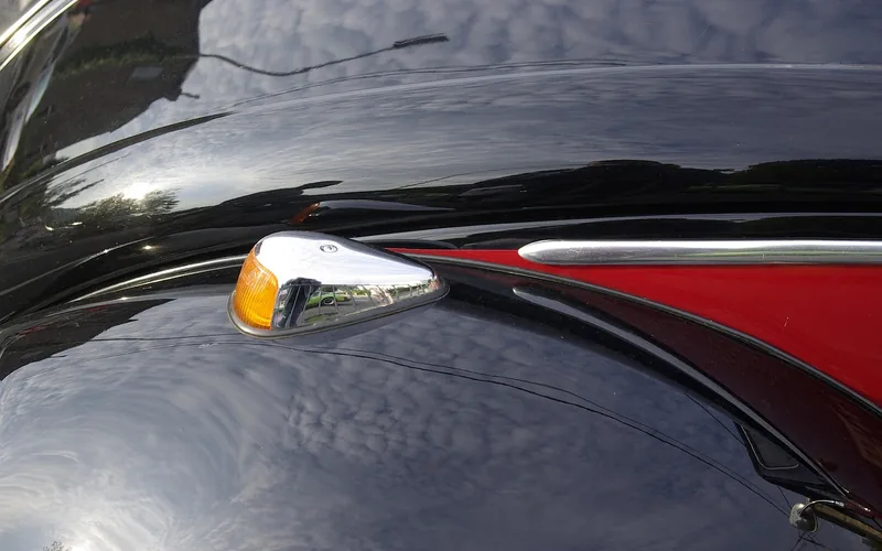 Glossy black painted fender with a chrome turn signal reflecting the sky