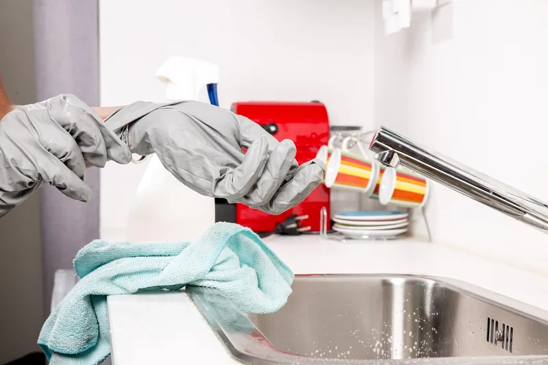 Gloved hands holding a cleaning spray bottle beside a microfiber cloth