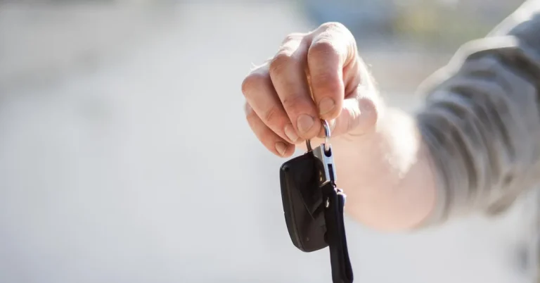 Hand holding a car key with a black plastic head on a split ring