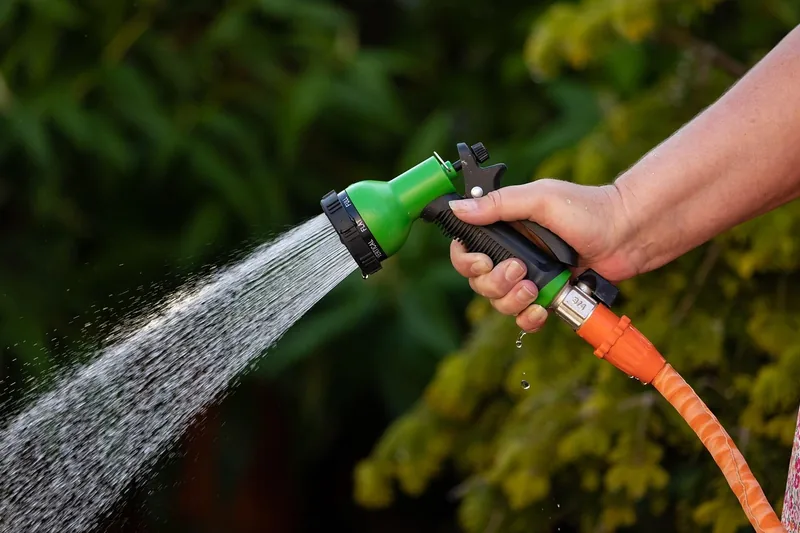 Hand holding a garden hose nozzle spraying a stream of water