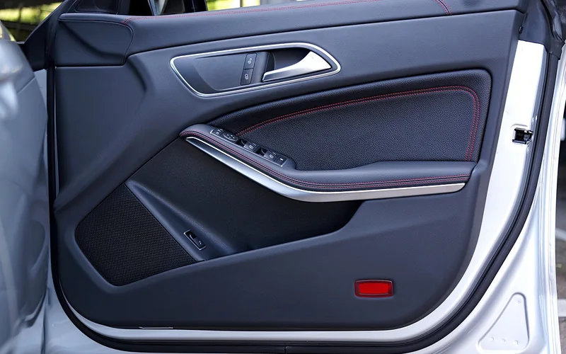 Open front car door showing the interior door panel, handle, window switches and speaker grille