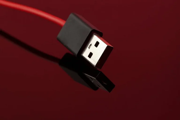 Red USB cable with a black connector resting on a reflective surface