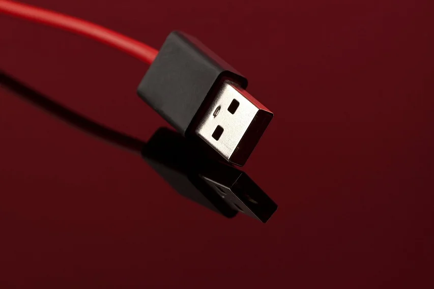Red USB cable with a black connector resting on a reflective surface