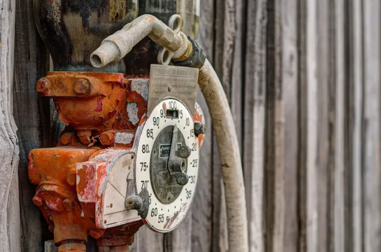 Weathered mechanical fuel pump with a dial gauge and hose on a wooden wall