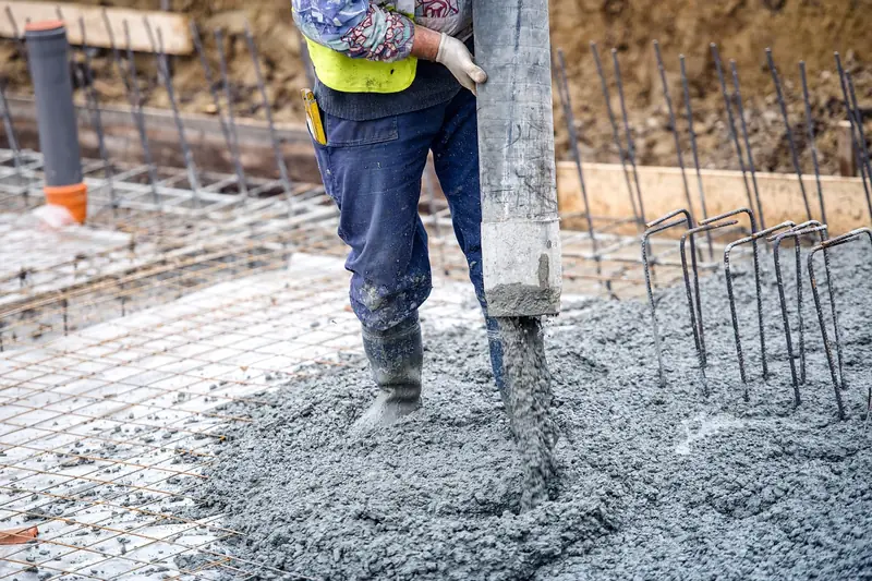 Wet concrete pouring from a pump hose onto a rebar grid at a construction site