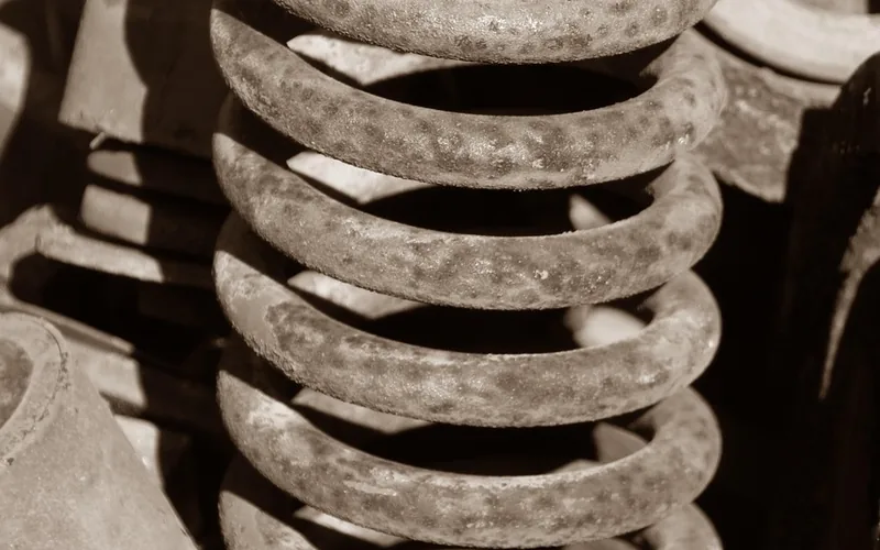 A rusty coil spring from a car suspension standing among other used parts