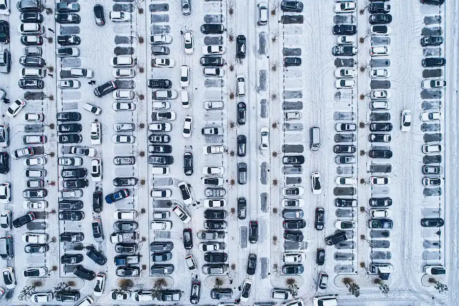 Aerial view of a snow-covered parking lot filled with rows of parked cars