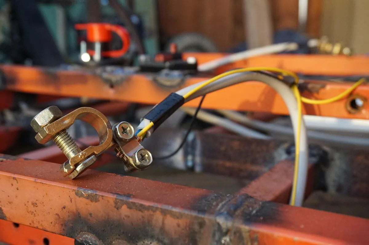 Brass battery terminal clamp with a bolt attached to a cable on an orange metal frame