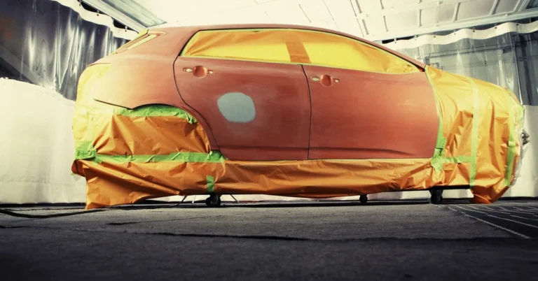 Technician spraying color-matched paint on a car body panel in a repair shop
