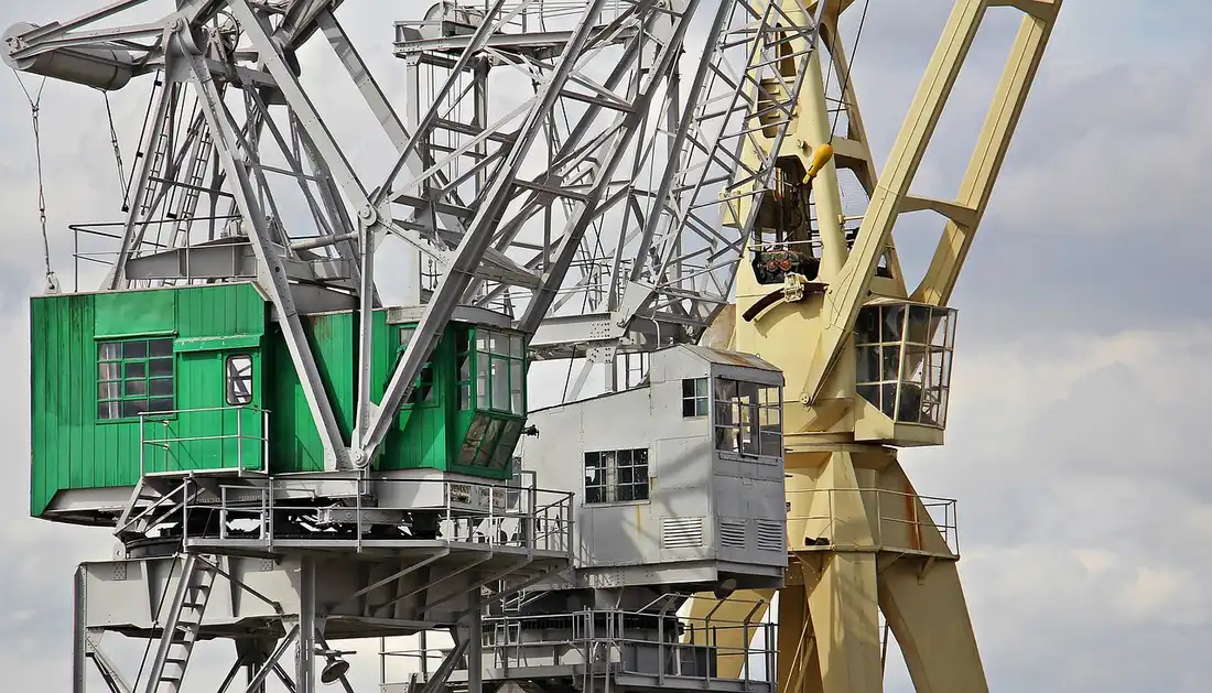 Harbor cranes with green and grey operator cabins against a cloudy sky