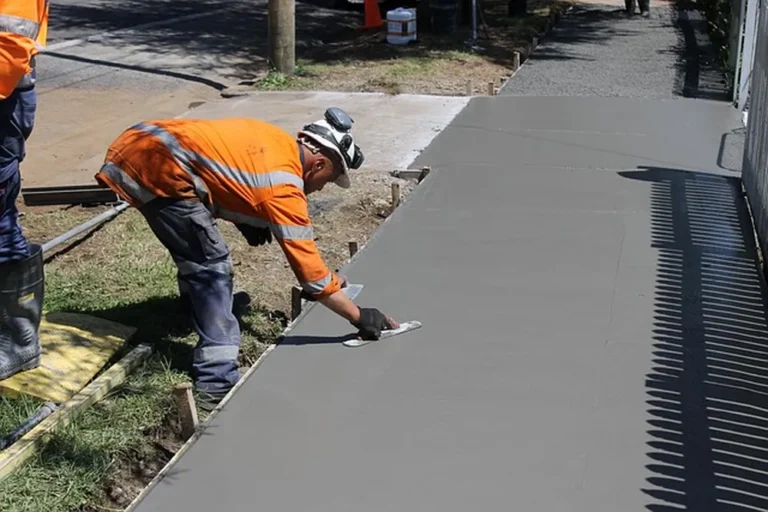 Worker in orange hi-vis clothing smoothing a fresh concrete path with a hand trowel