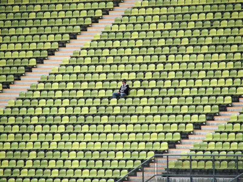 One spectator sitting in rows of empty green grandstand seats