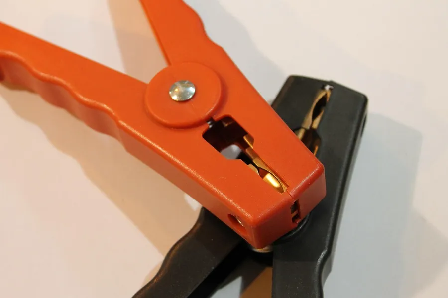 Orange and black jumper cable clamps with brass jaws on a white background