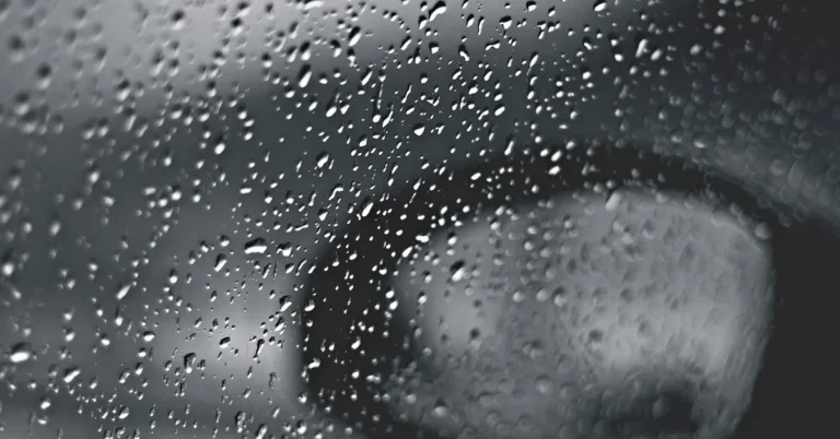 Raindrops on a car window with a blurred side mirror behind the glass