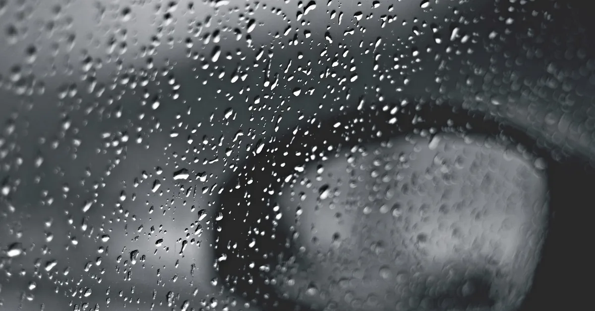 Raindrops on a car window with a blurred side mirror behind the glass
