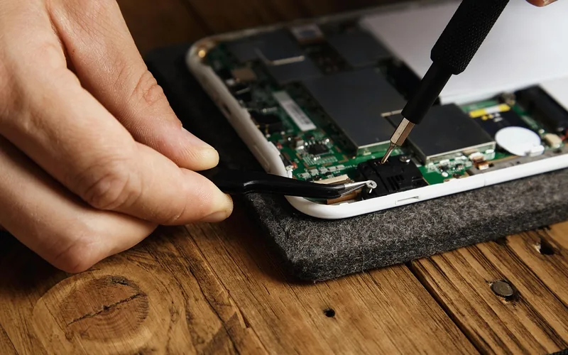 Hands using tweezers and a small screwdriver on an electronics circuit board