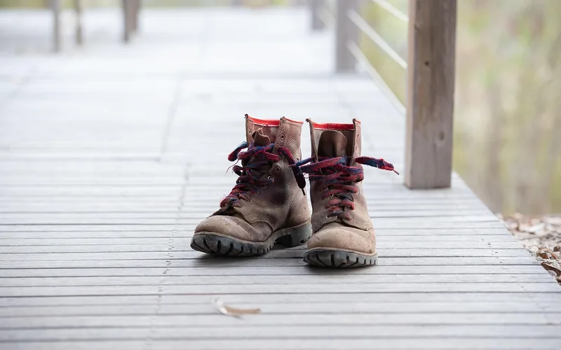 Worn brown leather work boots on a wooden deck, showing the same stiff-to-broken-in journey as a new Carhartt jacket