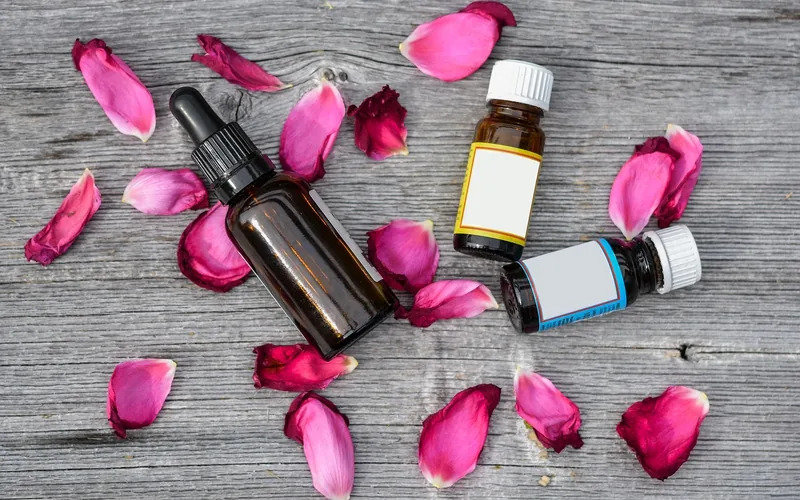 Amber glass essential oil dropper bottles surrounded by dried rose petals on a wood surface Amber glass essential oil dropper bottles surrounded by dried rose petals on a wood surface