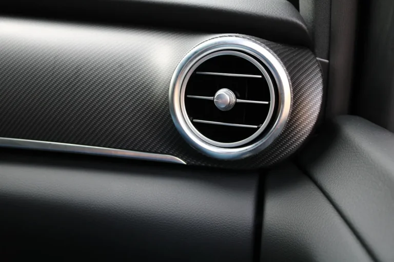 Round dashboard air vent with metal ring and adjustable slats inside a car cabin