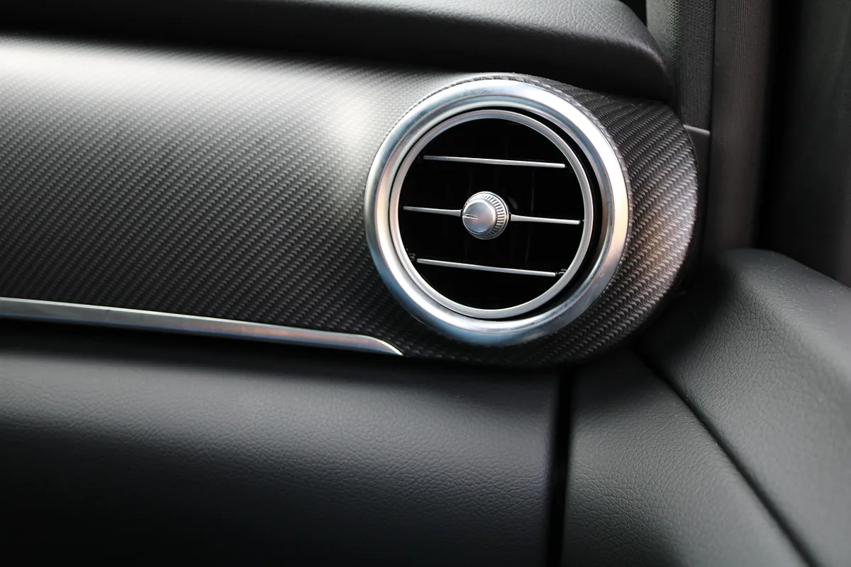 Round dashboard air vent with metal ring and adjustable slats inside a car cabin