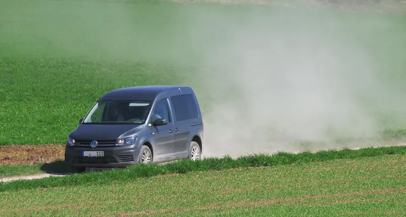 Van driving on a dusty field road, raising a cloud of dust