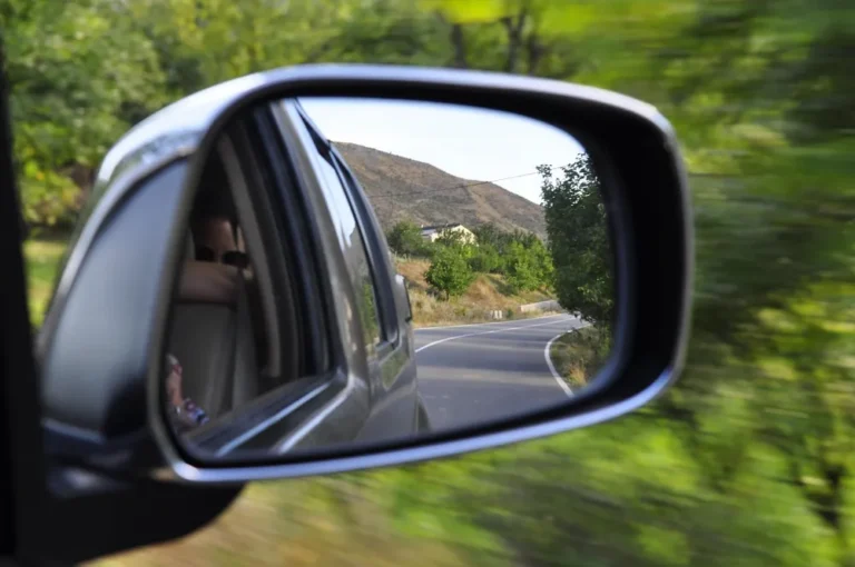 Car side mirror reflecting a country road with trees